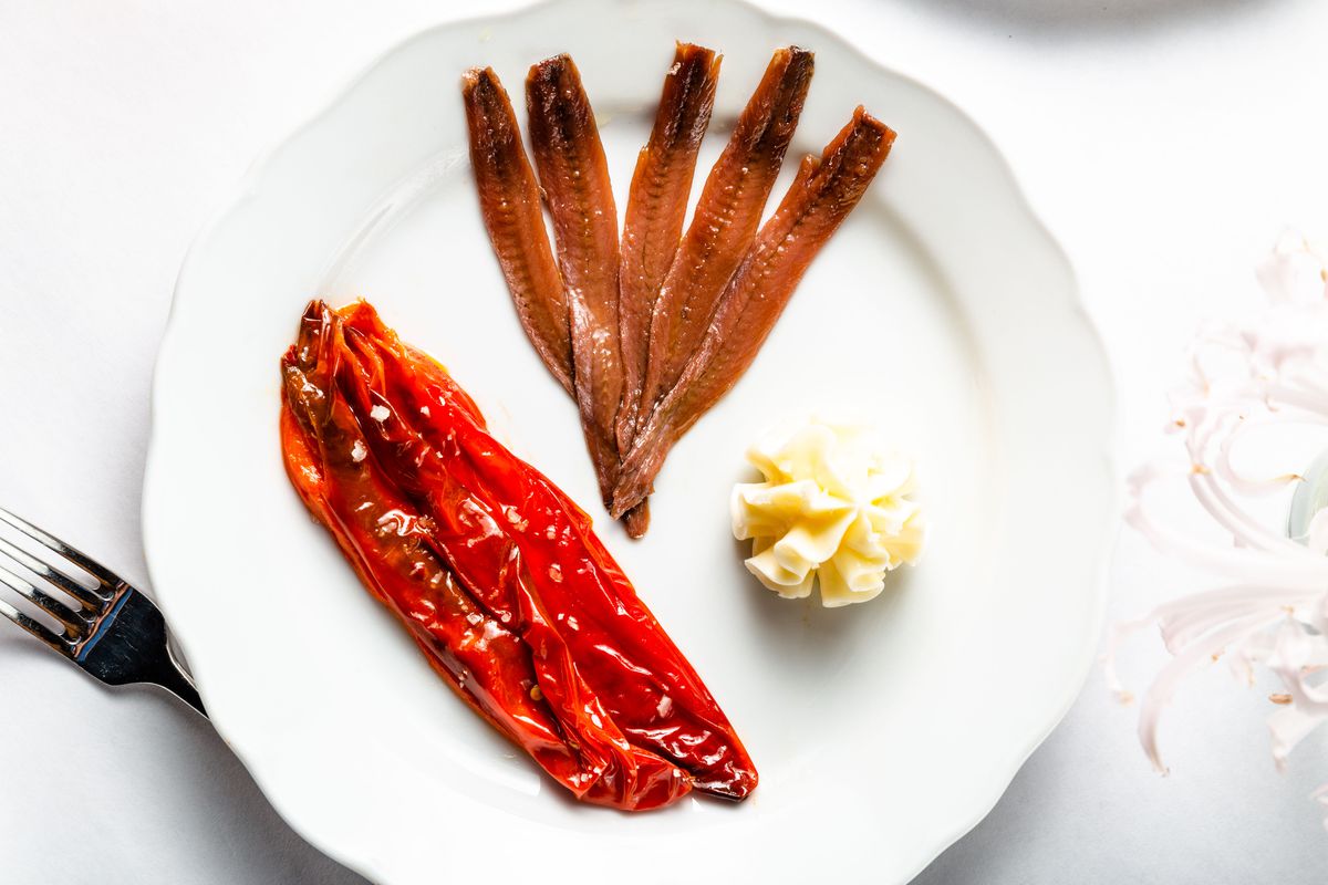 Roasted red peppers, a pat of butter, and five anchovies sit on a white plate