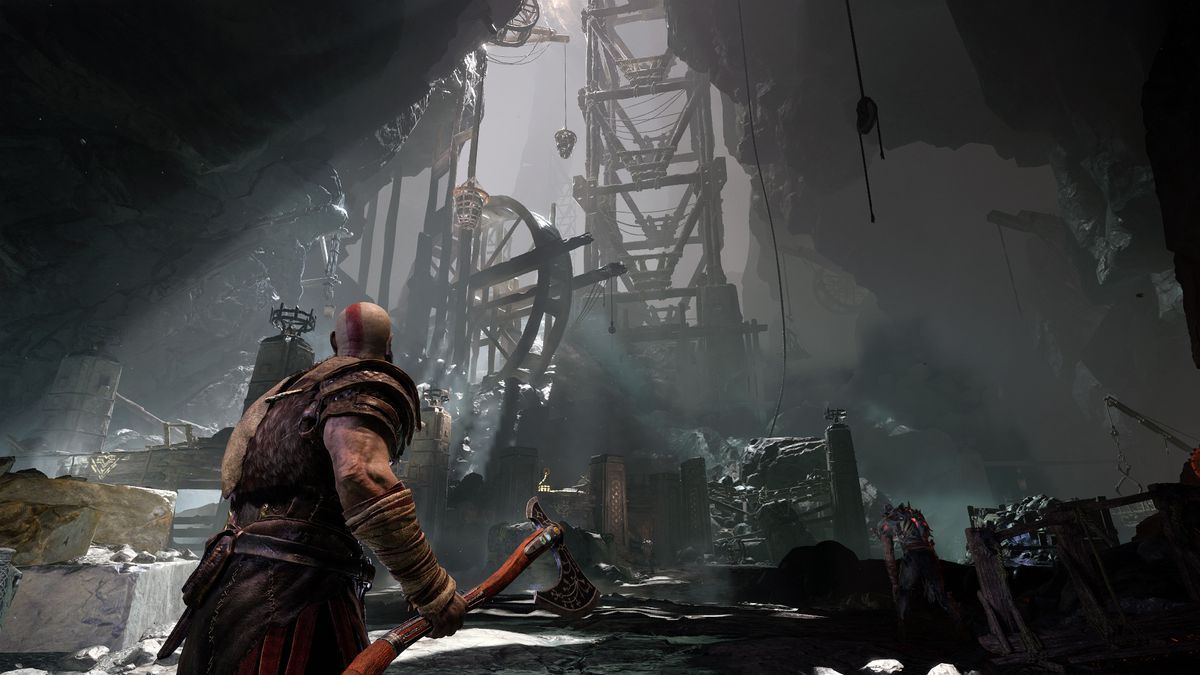 God of War - Kratos looks up at a large wooden contraption in a cave illuminated by a shaft of light