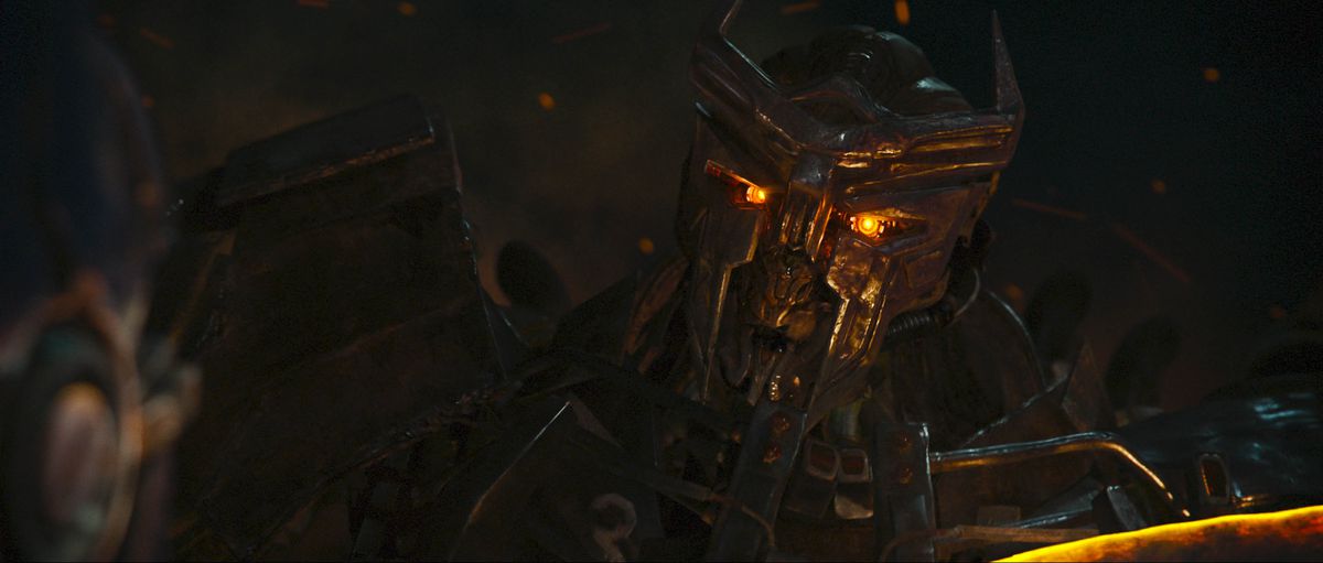 Scourge, a rusty-looking, intimidating Transformer with glowing orange eyes, seen in close-up in Transformers: Rise of the Beasts