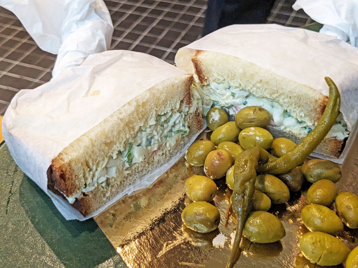 Two sandwich halves wrapped in white paper with olives in the center.