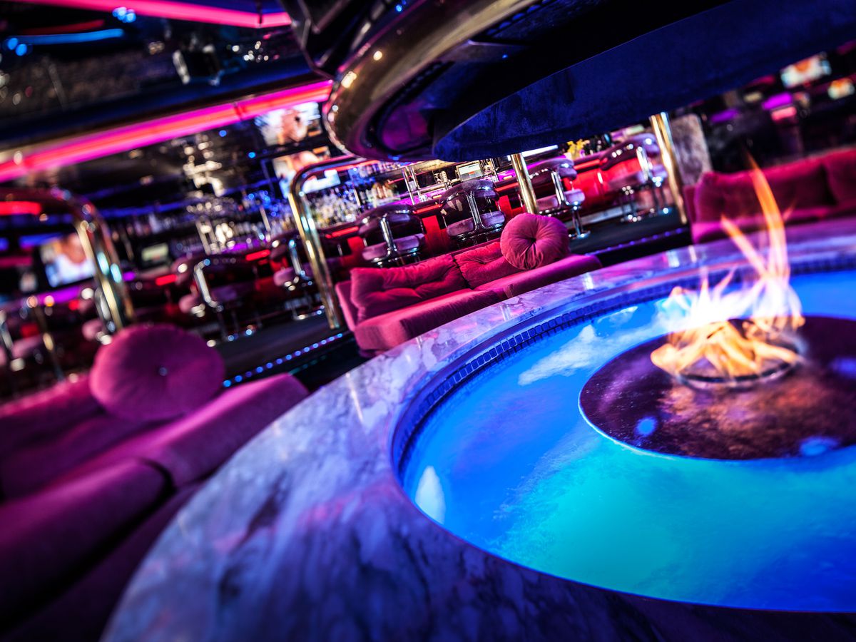 A neon-lit bar with a water feature with fire. 