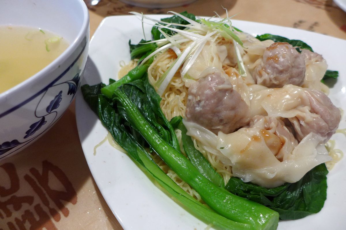 A bowl of broth is seen on one side, a pile of wontons and noodles on the other, framed in green bok choy...