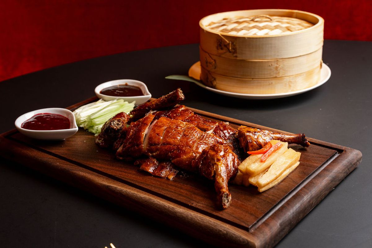 A wooden platter with sliced up roasted duck, served with cucumber slices and sauces.