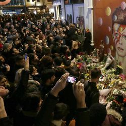 FILE - In this Monday, Jan. 11, 2016 file photo people gather next to tributes placed near a mural of British musician David Bowie by artist Jimmy C, in Brixton, south London. Bowie, the other-worldly musician who broke pop and rock boundaries with his creative musicianship, nonconformity, striking visuals and a genre-spanning persona he christened Ziggy Stardust, died Jan. 10, 2016.