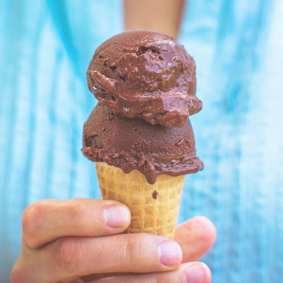 Two chocolate scoops on a mini cone held by someone in a blue shirt