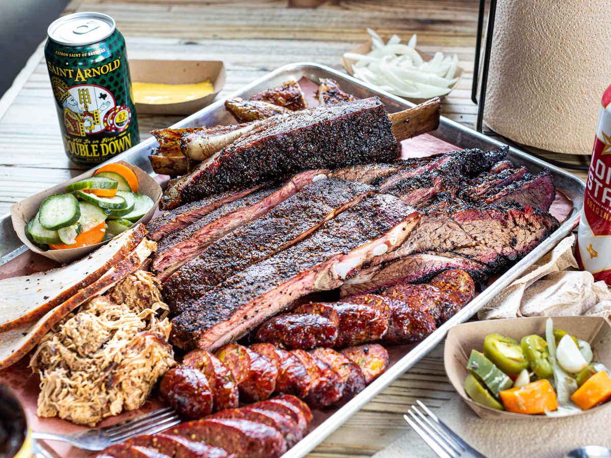 A spread from the Pit Room including brisket, sliced sausage, ribs, and traditional accompaniments on a barbecue tray.