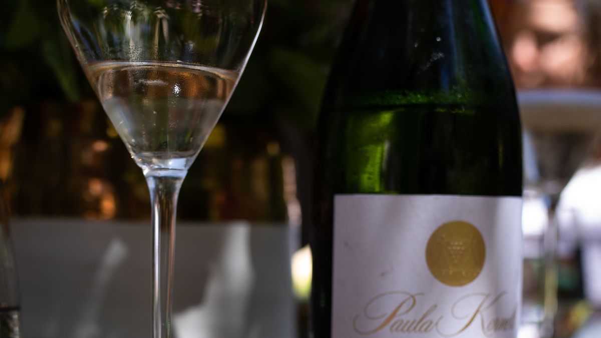 A bottle of sparkling wine on a table next to a glass.