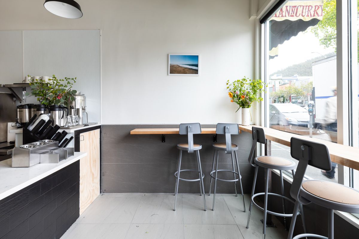 A sparse space with black lower walls and white upper walls, a simple wooden bar rail, and metal chairs.