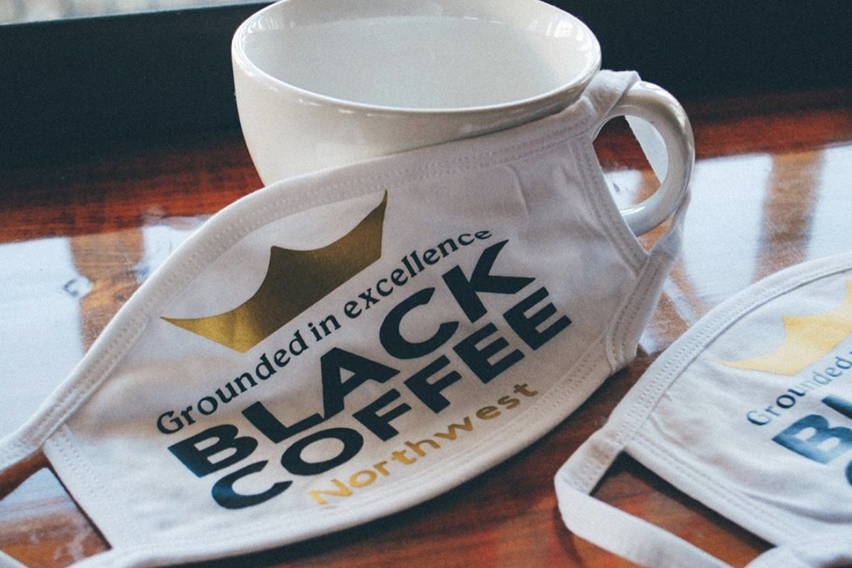 A face mask with “Black Coffee NW” written on it next to an empty coffee mug
