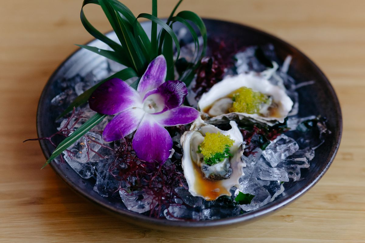 Two plump oysters topped with green onions and tiny lime green fish eggs sit in a bowl of ice.