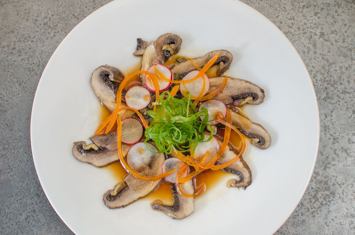 Overhead view of thinly sliced mushrooms arranged in a circle topped with thin carrot ribbons and radish rounds.