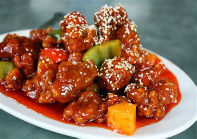 Cubed pork in a heavy sauce piled on a serving plate with cubed peppers and pineapple, and covered in sesame seeds