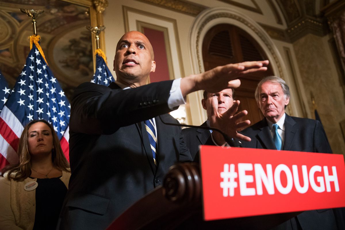 Senator Cory Booker speaking from behind a podium bearing a sign that reads, “#Enough.”