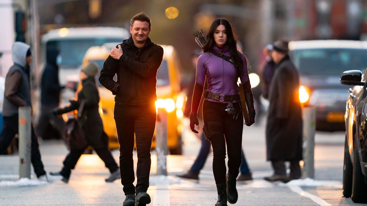 Jeremy Renner (L) and Hailee Steinfeld are filming a scene for ‘Hawkeye’ in the East Village in New York City. Renner is wearing black, whil Steinfeld has a purple athletic jacket and a bow hanging from her shoulder. 