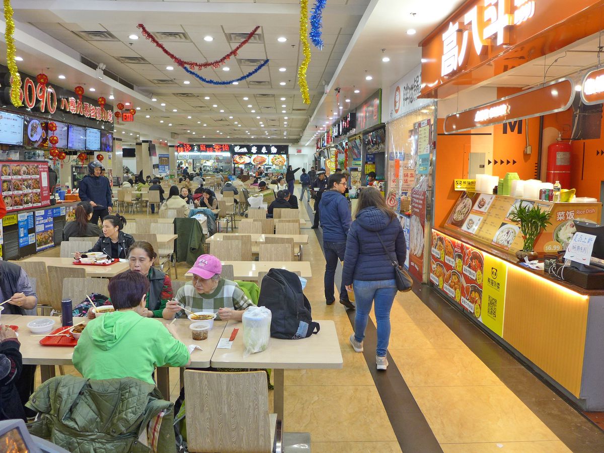 A brightly lit food hall with stalls on either side and tables in the middle.