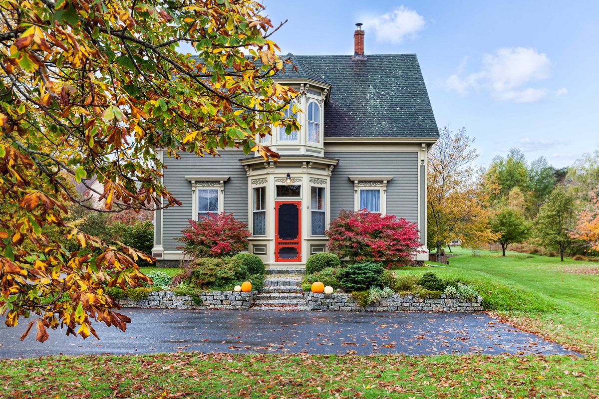 A gray house with victorian features in the fall. 