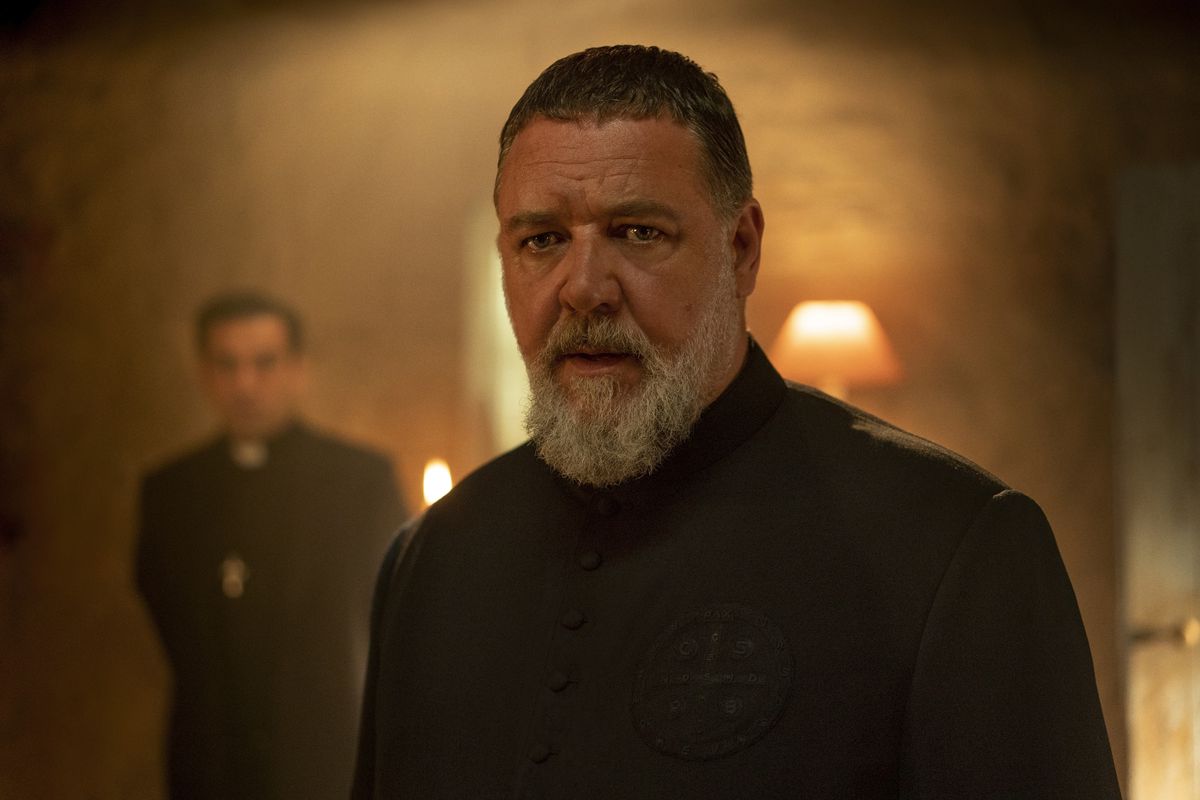 Russell Crowe as Father Gabriele Amorth in The Pope’s Exorcist facing the camera with short hair and a glowing orange light behind him