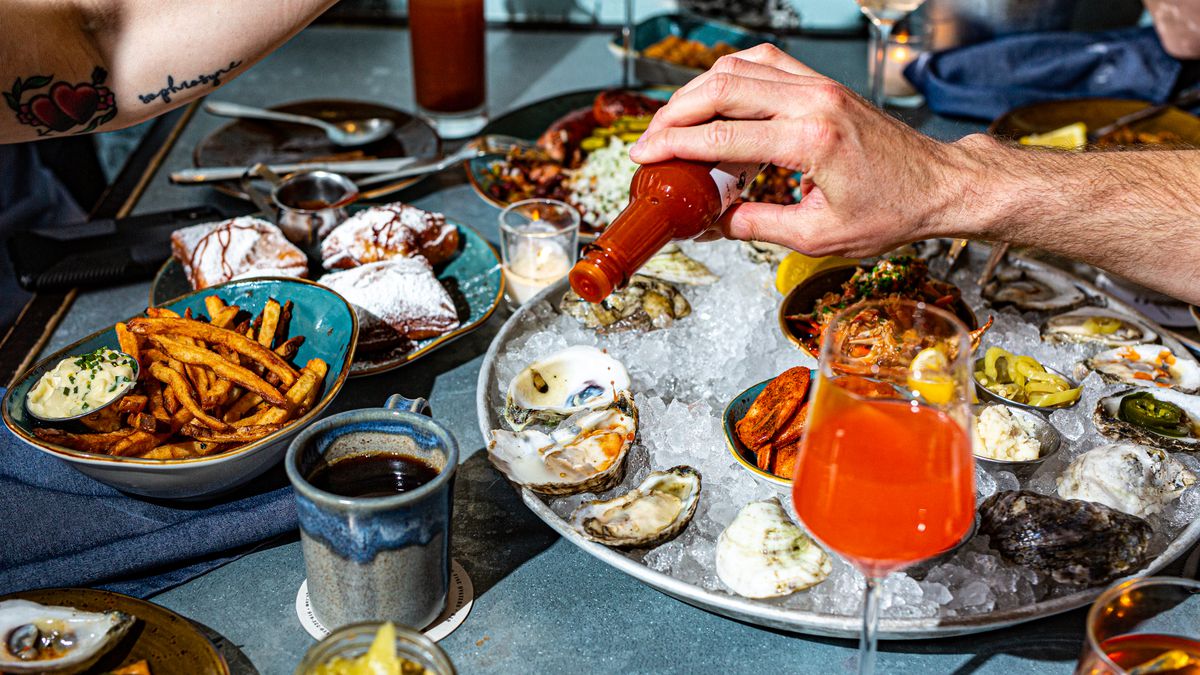 A white hand pours hot sauce onto a plate of oysters.
