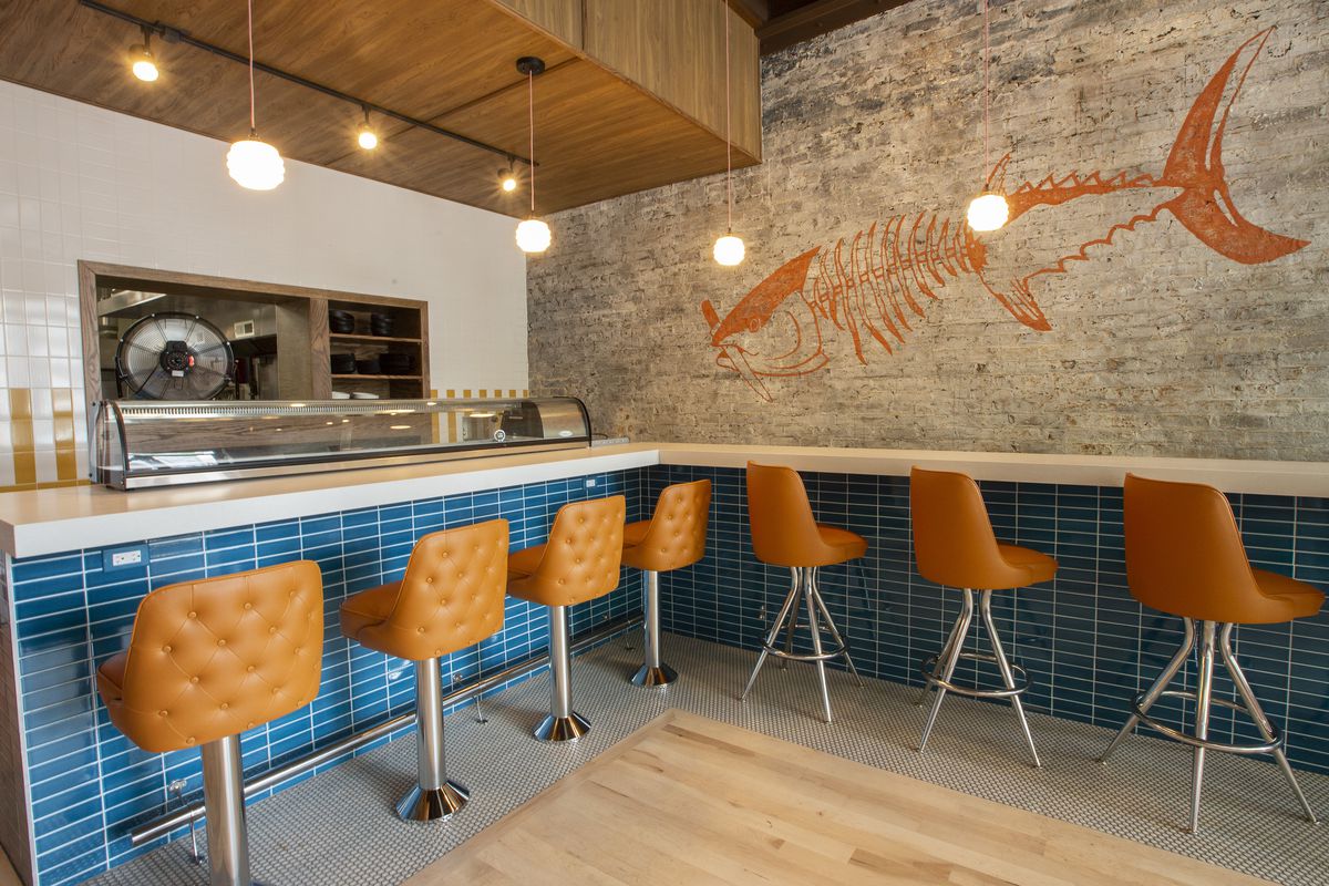 An L-shaped sushi bar with blue tile and orange upholstered stools.