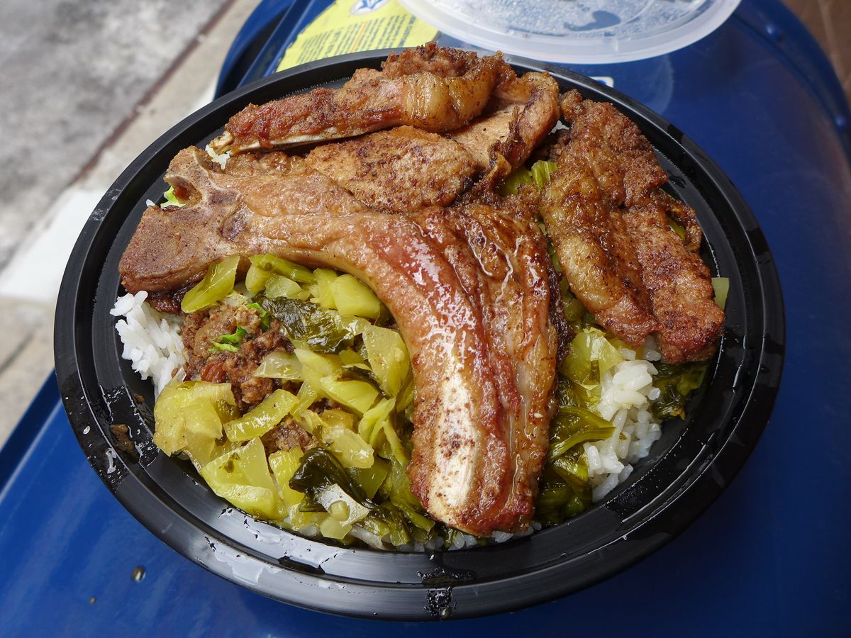 A pile of pork chops on rice in a round black plastic container.