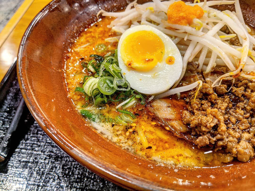 Closeup on a bowl of ramen with an opaque yellow broth, soft boiled egg, ground pork, and bean sprouts.