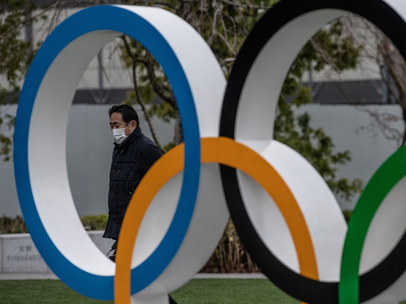 The picture is a closeup of a statue featuring the Olympic Rings in Tokyo. A man is pictured walking by wearing a mask to protect from the coronavirus With the Olympics just a few short weeks away, and dependent on a successful vaccine drive, the mood is pretty gloomy.