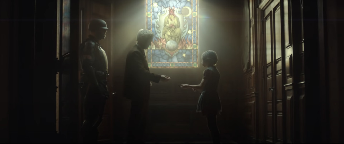 Flanked by a guard, Mobius M. Mobius passes something to a small child, in front of a stained glass window of a devil-like figure in Loki.