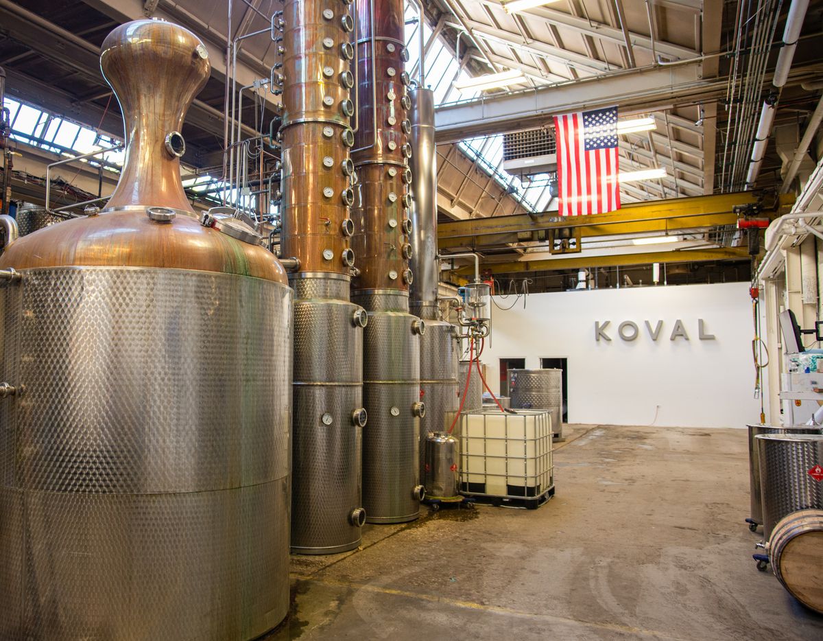 Several enormous metal distilling tanks inside a warehouse space. An American flag hangs vertically from the ceiling.