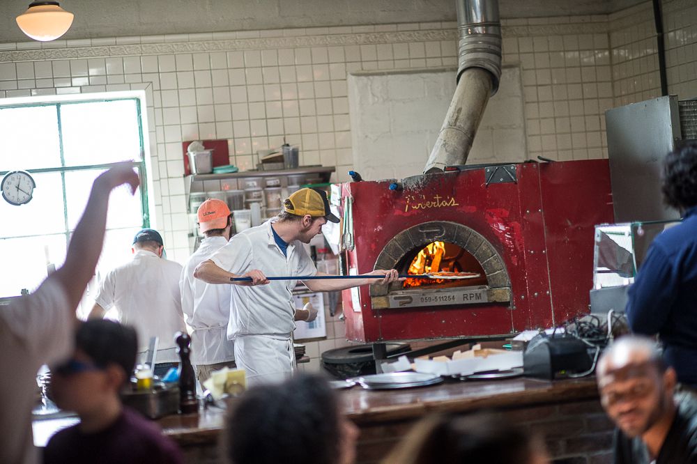 A man inserts a pizza into a red wood-fired oven.