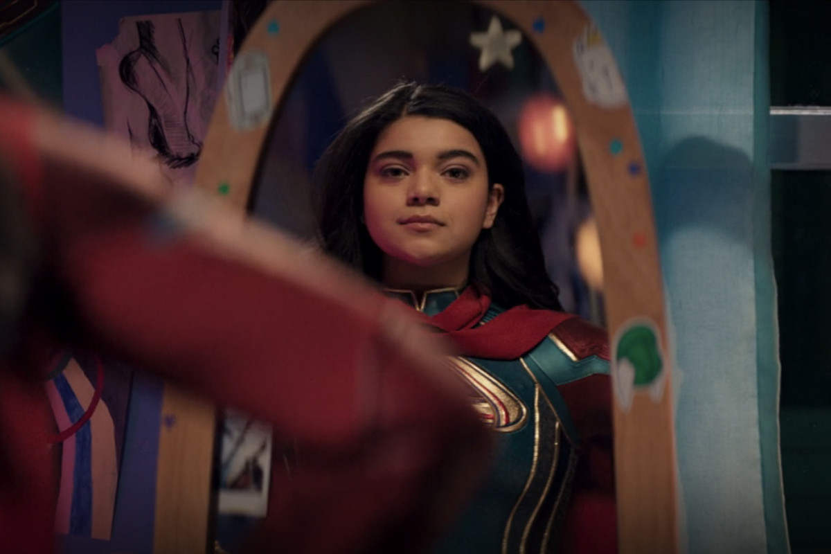 Kamala Khan/Ms. Marvel looks at herself in the mirror, smiling quietly and proudly at her superhero duds in Ms. Marvel. 