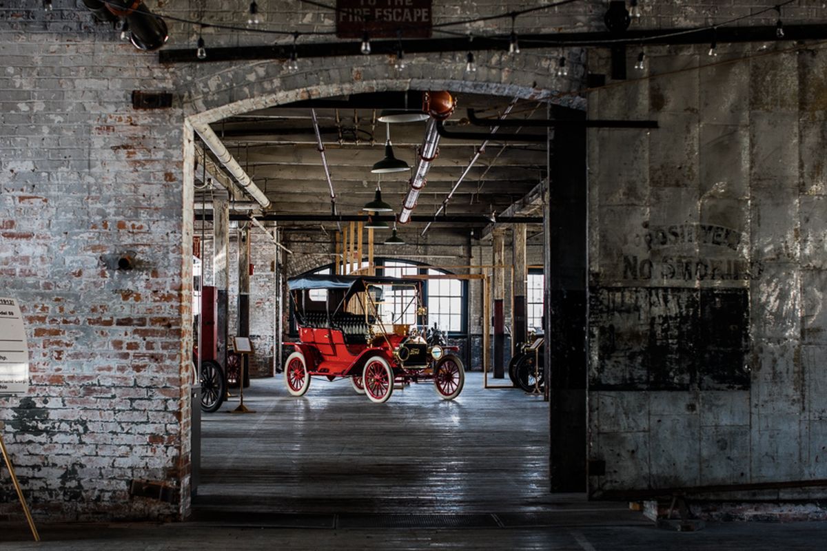 The interior of the Ford Piquette Avenue Plant in Detroit. The walls are steel and brick. There is an old red automobile on display.