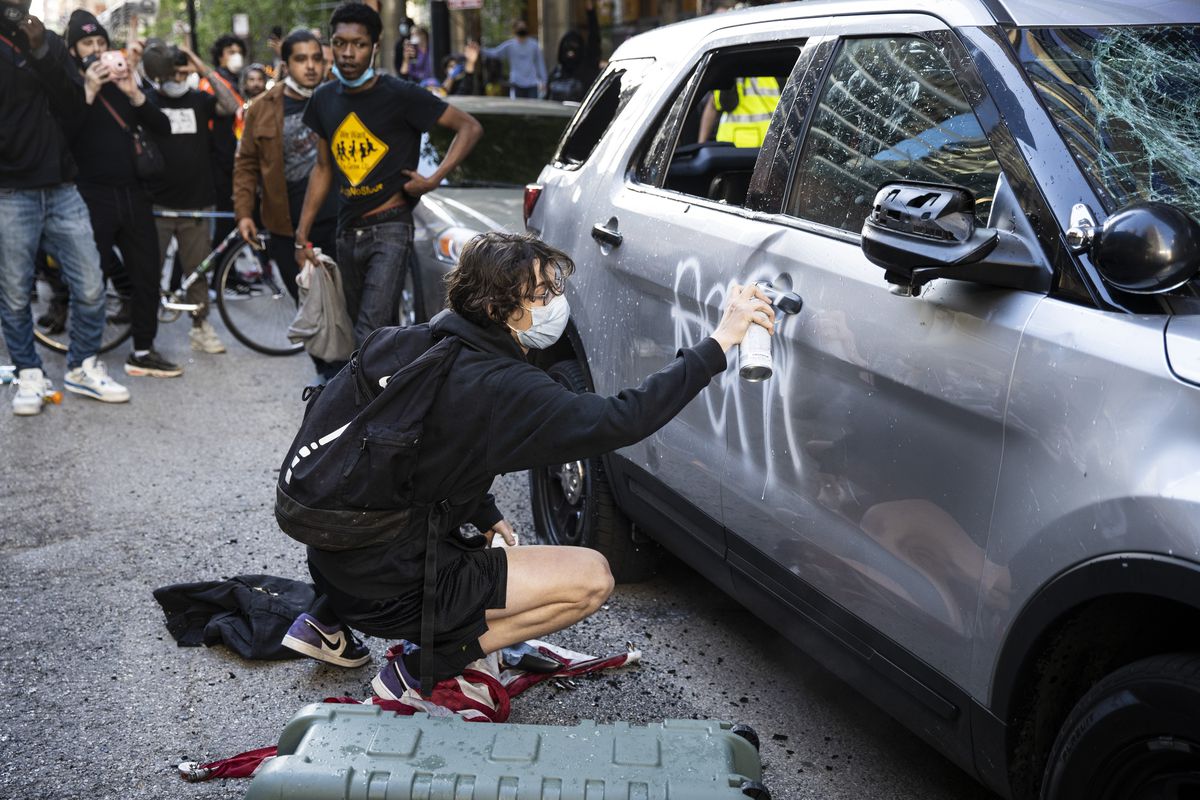A protester sprays paints on a Chicago Police Department SUV on Kinzie near State in Chicago, Saturday, May 30, 2020 as thousands of protesters in Chicago joined national outrage over the death of George Floyd.