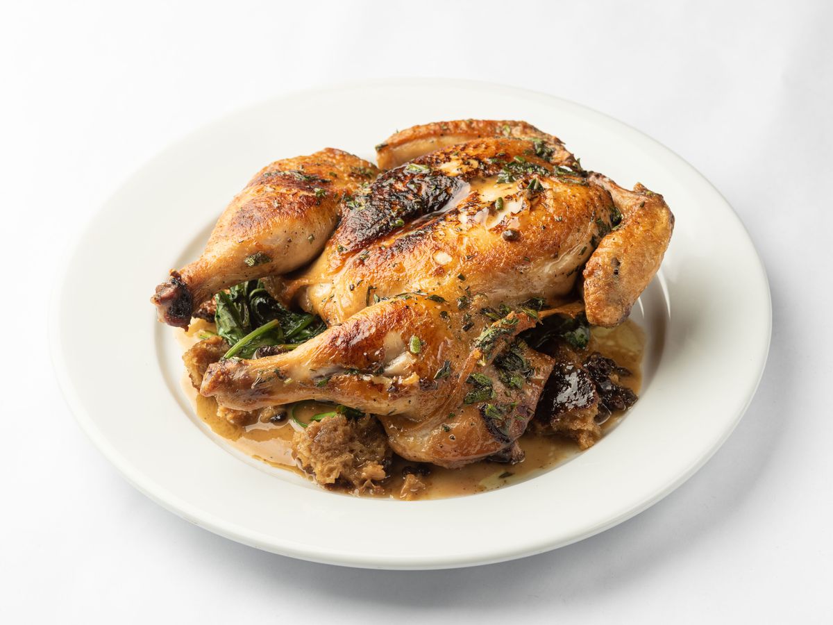 An angled photo on a white background of a plate with a full roasted chicken atop.