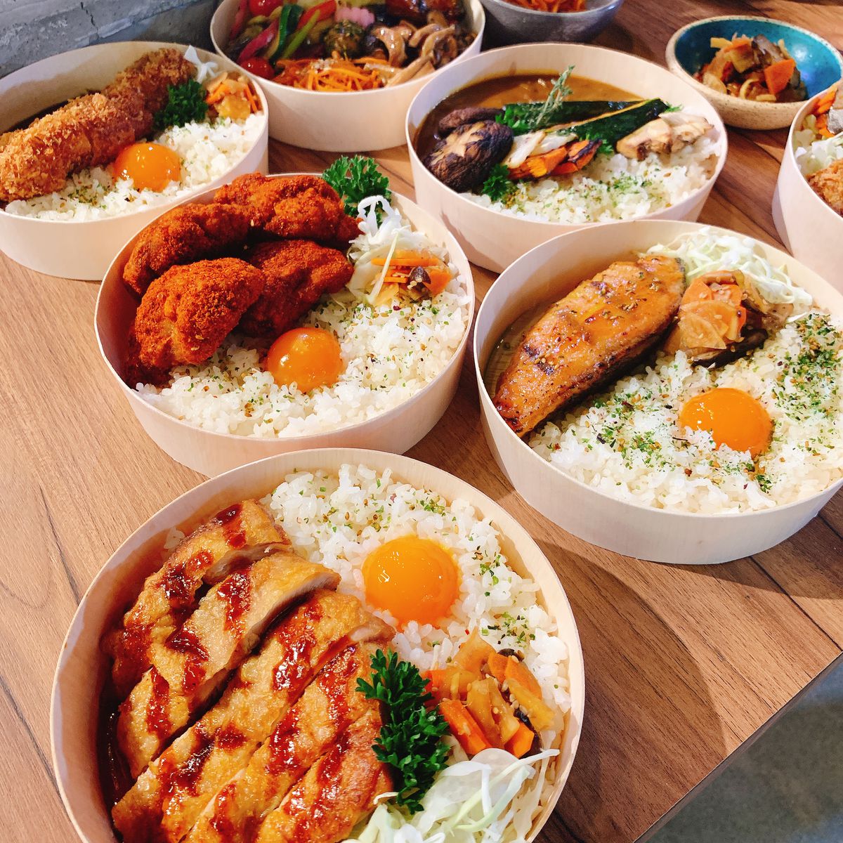 A variety of bento bowls with rice, egg yolks, fried chicken, and more.