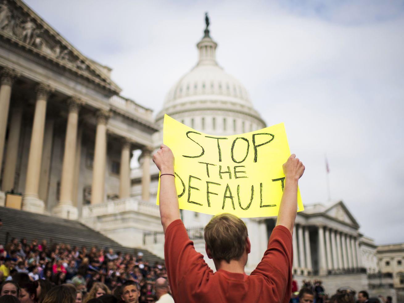A protester at the US Capitol building holds a hand-lettered sign over their head that reads “Stop the default.” 