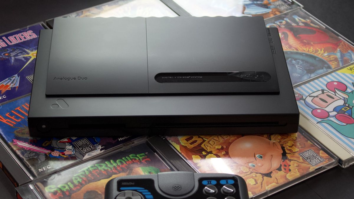 The Analogue Duo, on top of several game CD cases, and a blue and black controller beneath it