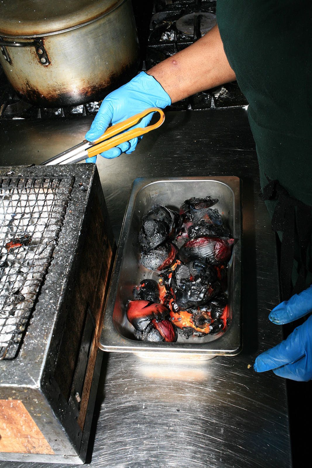 A gastro tray full of charred peppers, very blackened, next to a grill