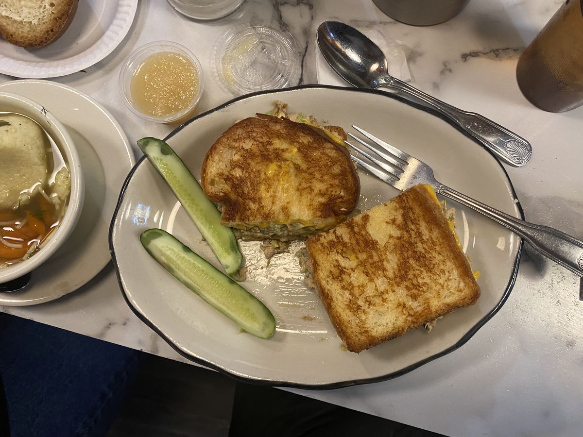 A tuna melt served on a white plate with pickles on the side.