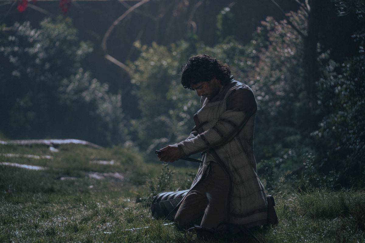 Ser Criston Cole holds a knife to his stomach in a grassy area in House of the Dragon.
