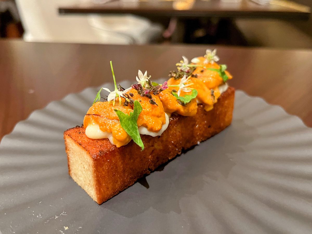 A rectangular cube of milk bread topped with uni, shiso, and little edible flowers.