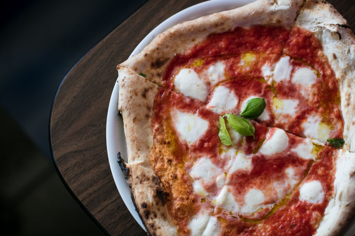a neapolitan pizza with mozzarella, red sauce, and fresh basil leaves in the center.