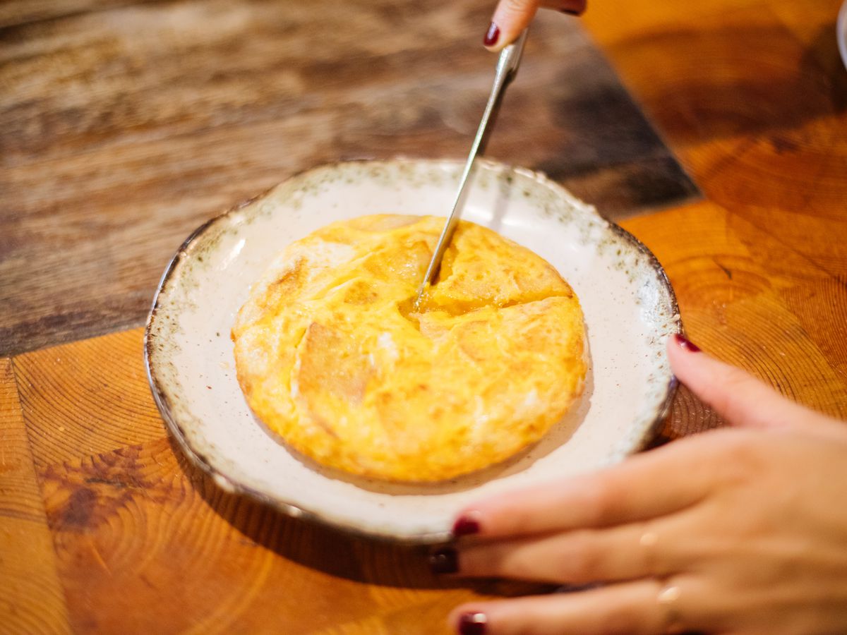 A knife cuts a wedge out of a spanish tortilla on a plate.