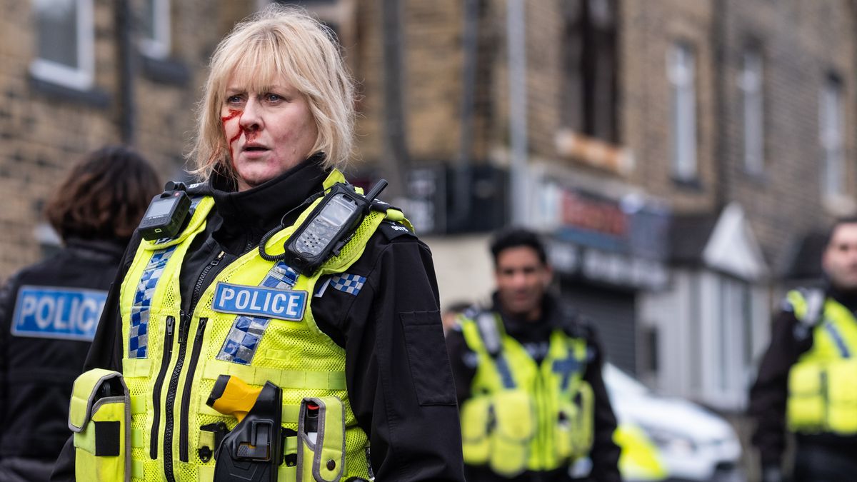 Sarah Lancashire as Sergeant Catherine Cawood in Happy Valley: a blond woman in late middle age wearing a high-viz police uniform with a bloodied face