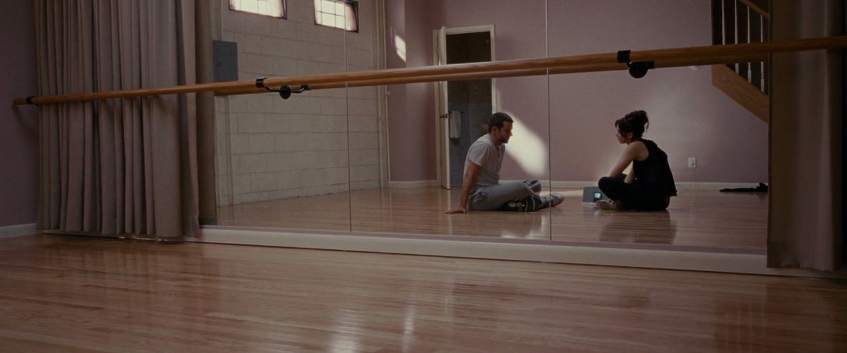 Jennifer Lawrence and Bradley Cooper sit on the floor of a dance studio, reflected in a mirror, in a screenshot from Silver Linings Playbook