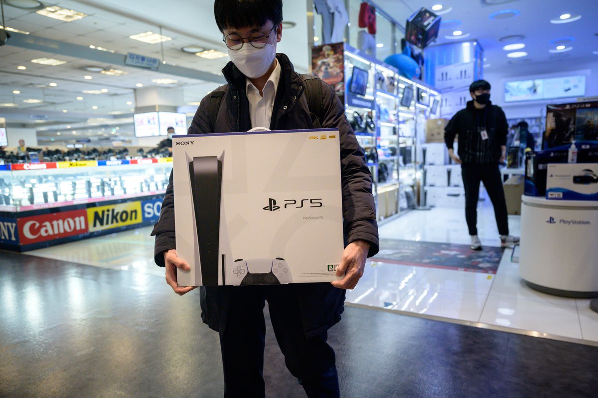 a man wearing a mask carries a PlayStation 5 out of a store