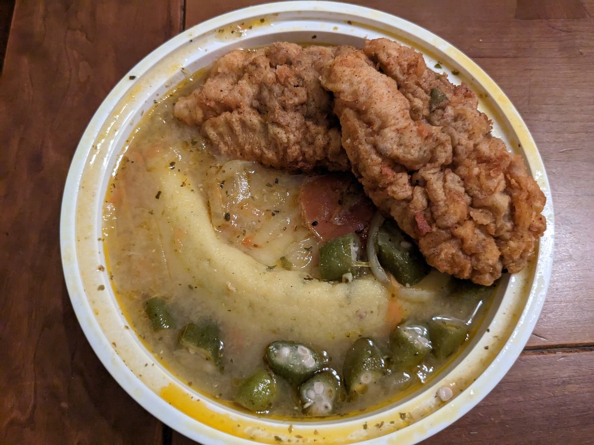 A white plastic dish with fried fish, blond gravy, and porridge with okra.