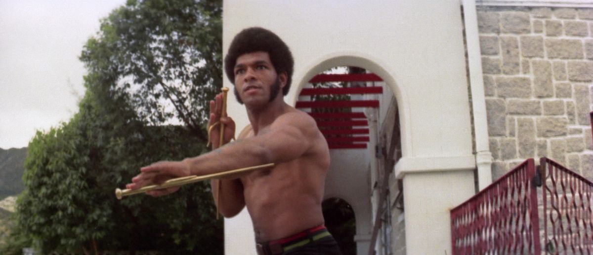 Ron Van Clief holds a pair of sai while shirtless and outside in The Black Dragon’s Revenge.
