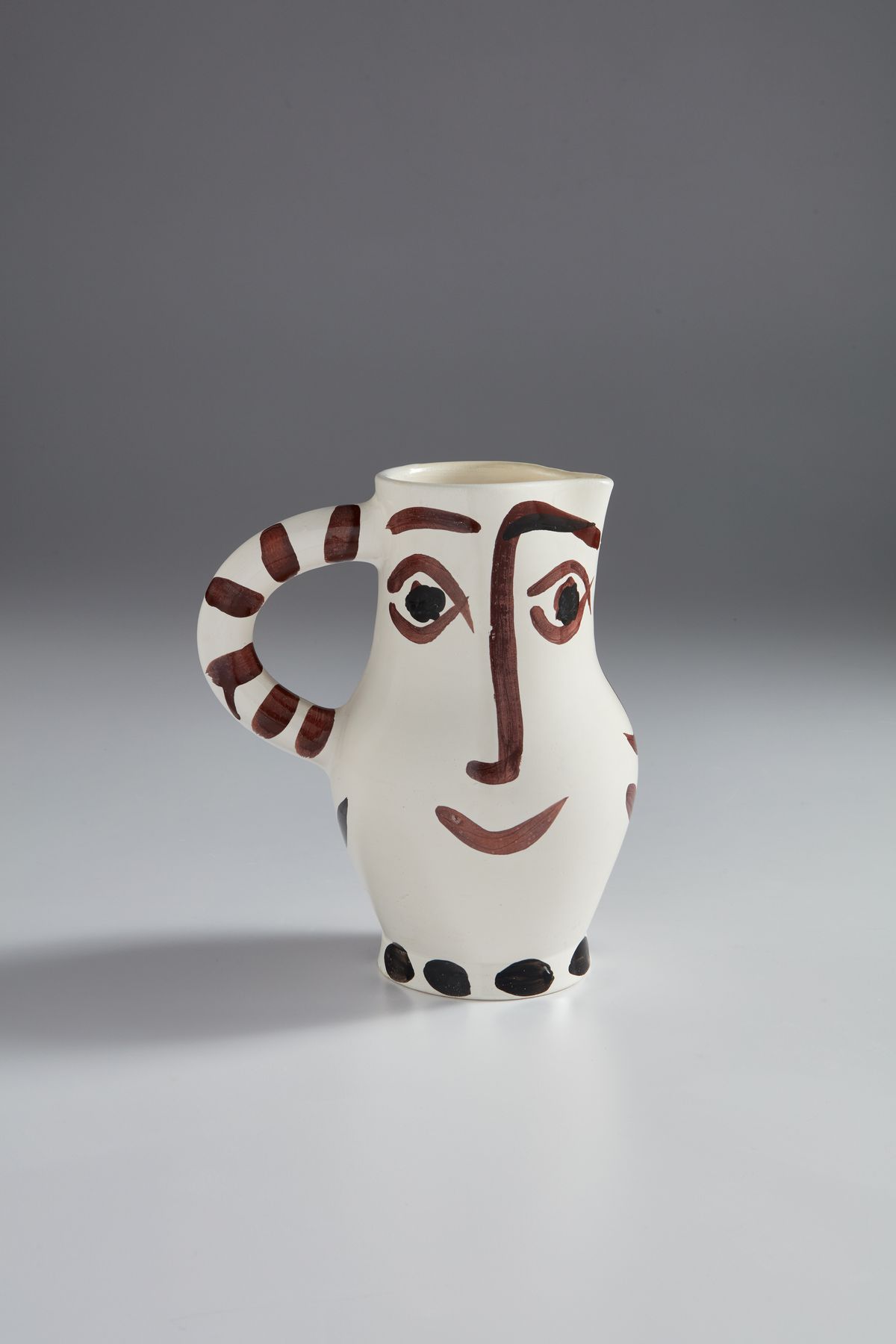A curved white vase with a face painted on the body.