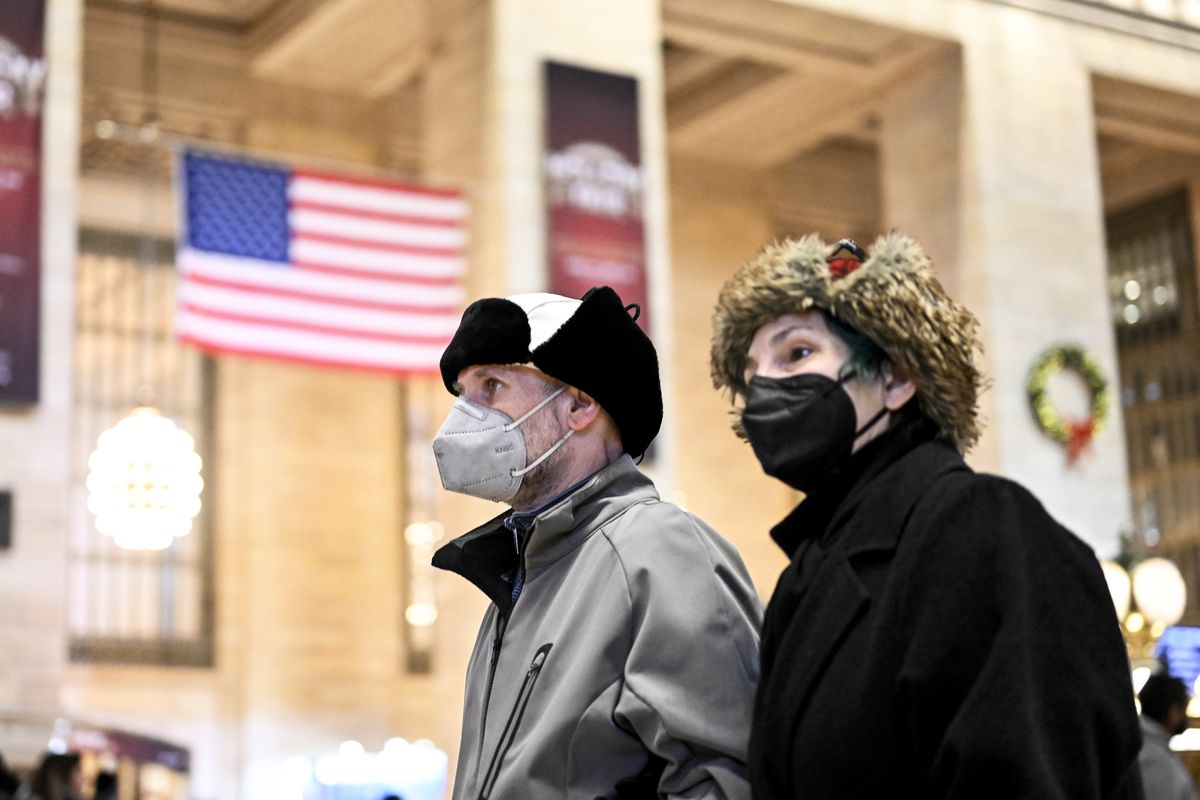 Masked pedestrians walk past a US flag in a streetfront window in New York City on December 12, 2022.