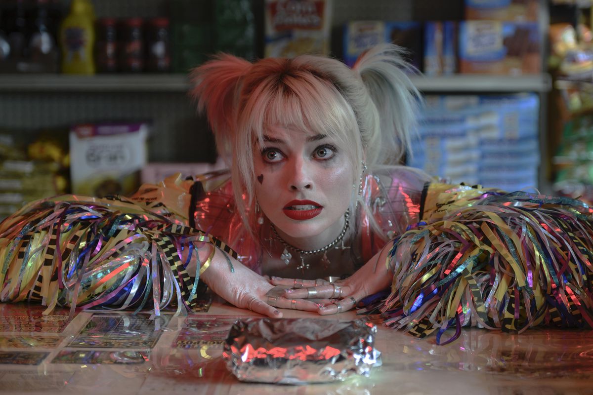 Margot Robbie rests her arms on a deli counter and looks pleadingly at her breakfast sandwich as Harley Quinn in Birds of Prey.